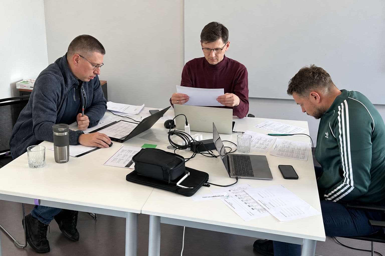 Trzech uczestników pracuje nad wydrukowanym scenariuszem i laptopami